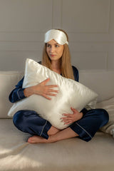 Silk closet ivory pillowcase set including eye mask and scrunchie. Woman holding pillow.