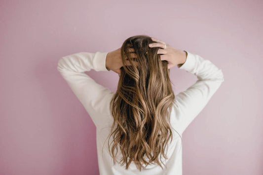 Woman standing with back to us and putting her hands through her hair