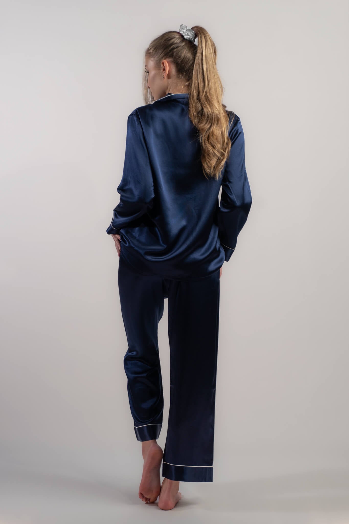 Woman wearing Silk Closet navy blue long pyjama set pants - sitting on couch. 100% mulberry silk. Back view.